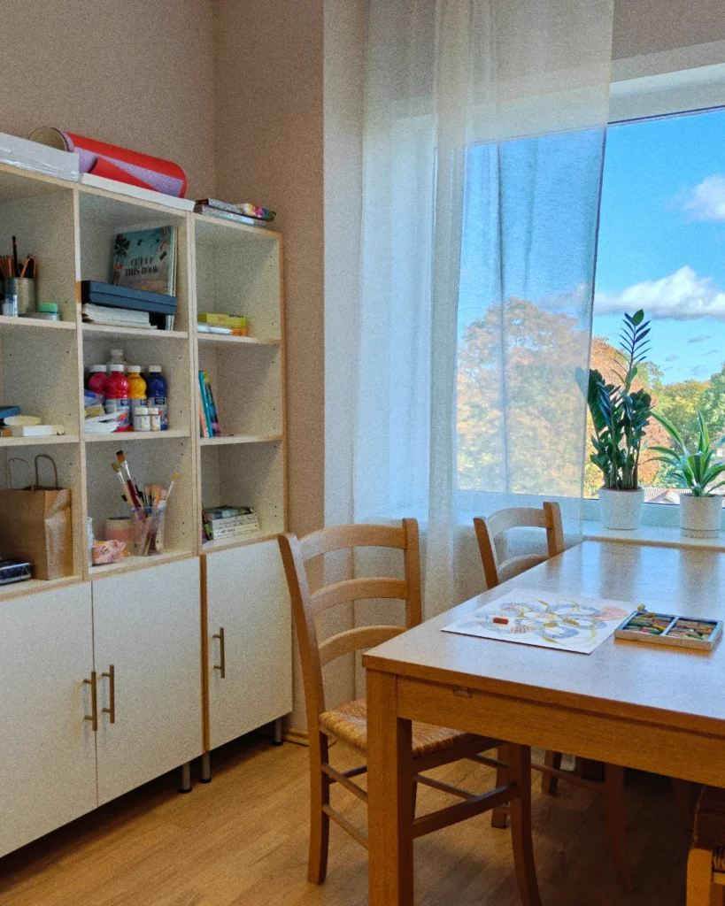 Loovterapeudi tööruum valge riiuli ja lauaga akna all